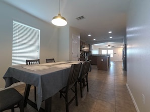 A dining area with a table set for four, a kitchen in the background, and a hallway leading to other rooms.