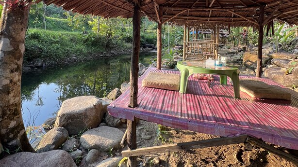 Un espacio de estar rústico al aire libre con techo de paja, una mesa pequeña y bancos.