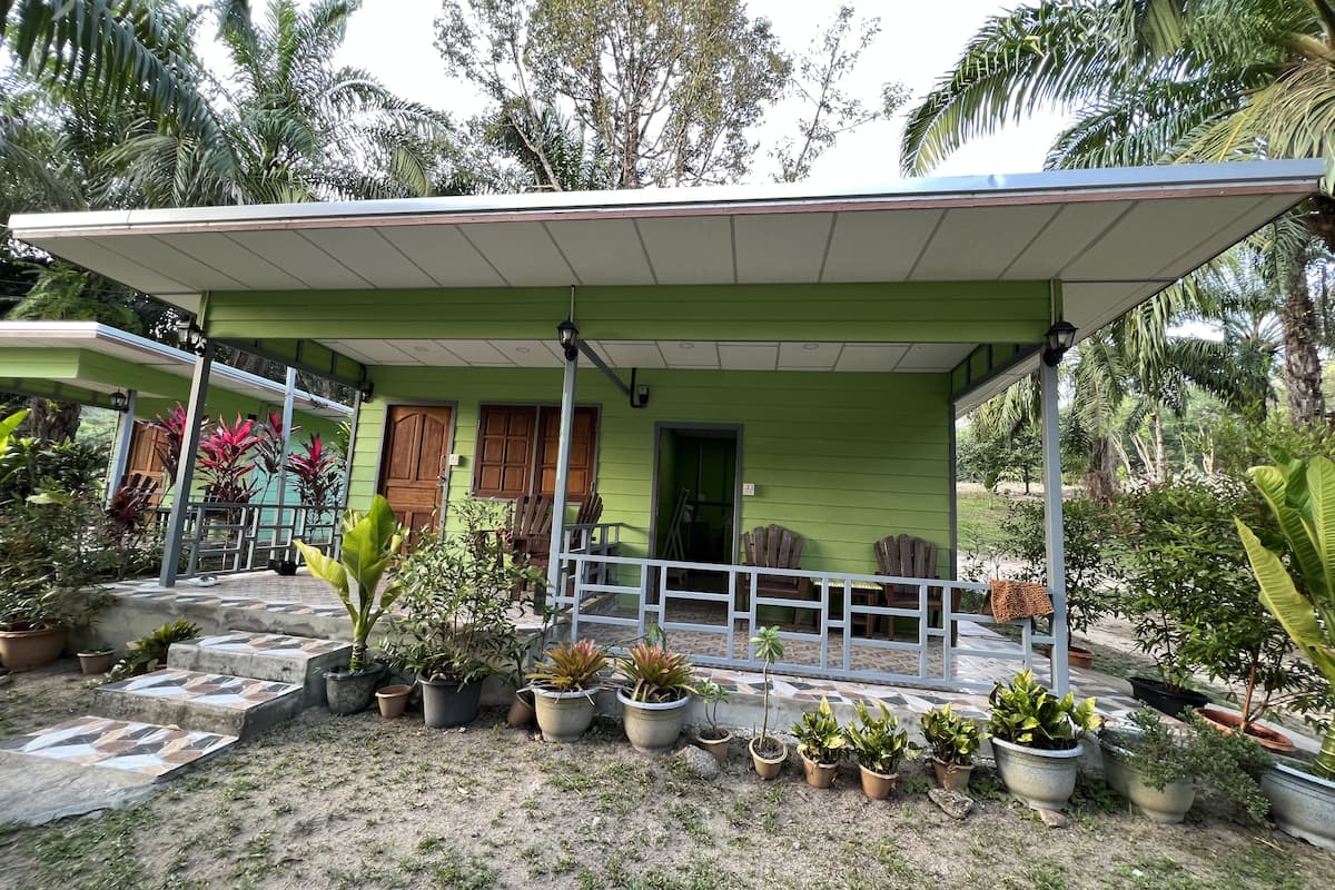 A green house with a covered porch, potted plants, and wooden chairs.