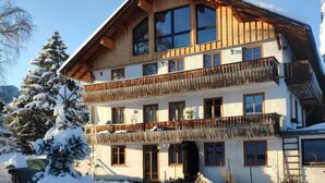 A multi-story wooden chalet with balconies, surrounded by snow-covered trees and a clear sky. - Haus am Weißbach - Vacation in the Pfronten Valley (Pfronten)