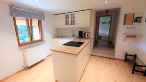 A modern kitchen with a central island, white cabinetry, and a window with a striped valance. - Haus am Weißbach - Vacation in the Pfronten Valley (Pfronten)