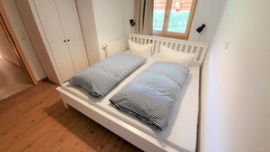 A bedroom with a bed, a wardrobe, a window, and a lamp. - Haus am Weißbach - Vacation in the Pfronten Valley (Pfronten)
