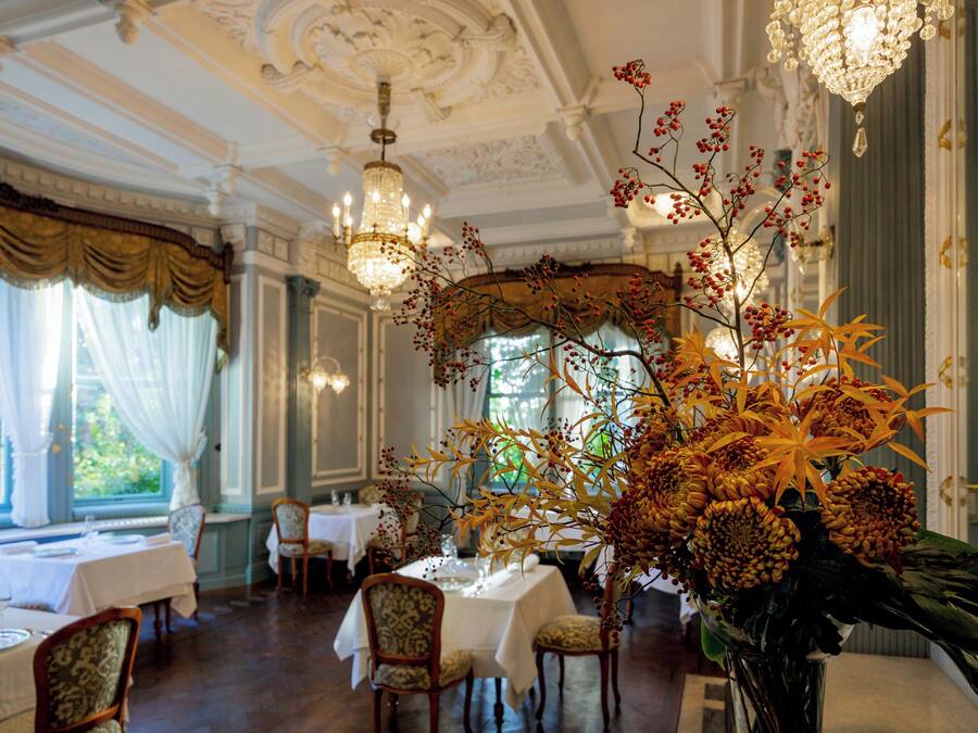 A dining area with tables set for service, chandeliers, and a large floral arrangement.