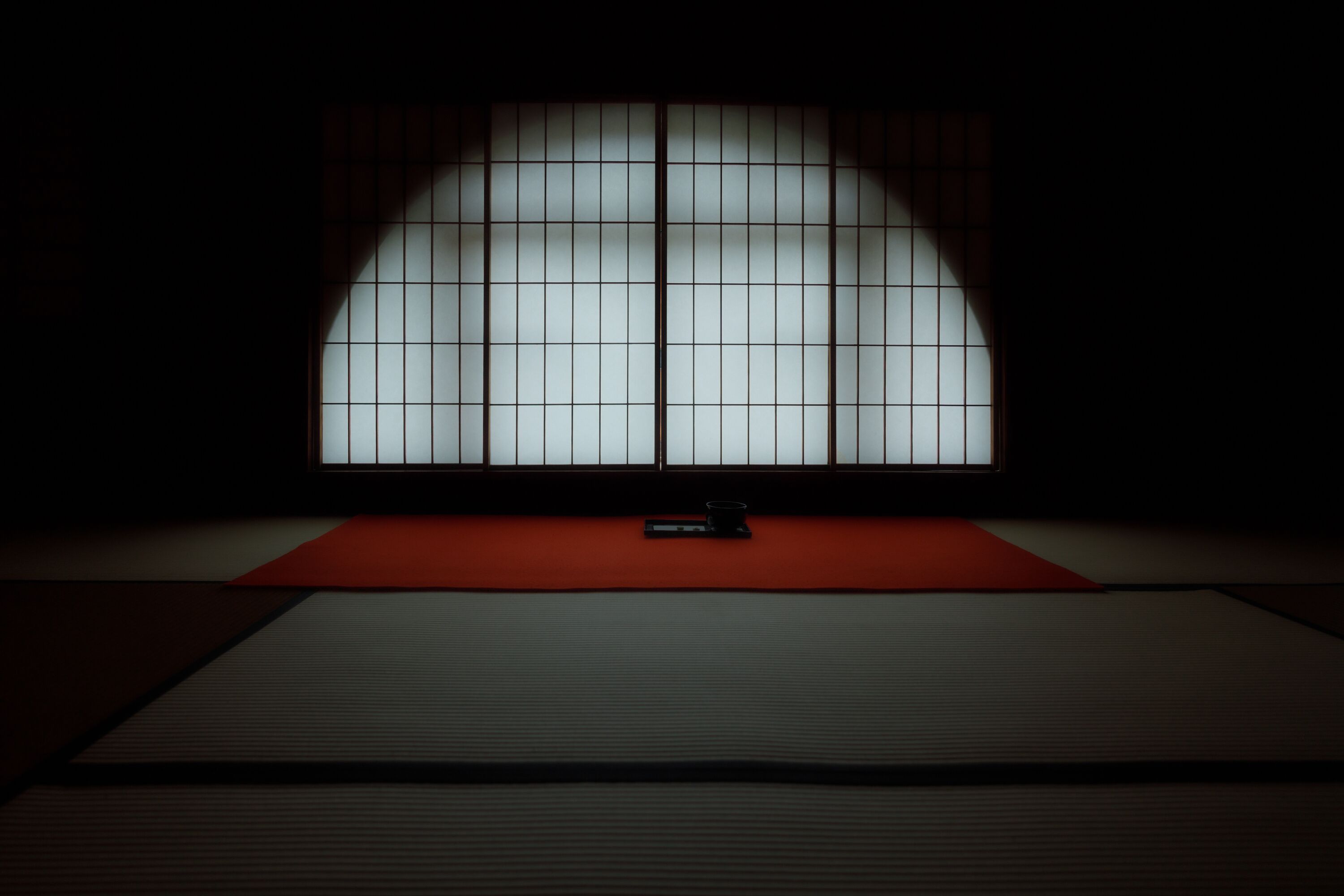 A tatami mat room with a shoji screen, a low table, and a red mat.