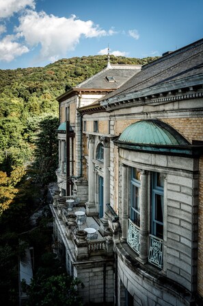 Un edificio histórico de arquitectura clásica, con columnas, una cúpula verde y un balcón que da a una ladera boscosa.