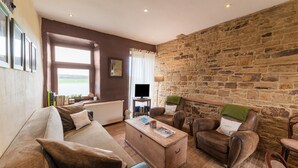 A cozy living room with a stone wall, a sofa, two armchairs, a wooden coffee table, and a television.