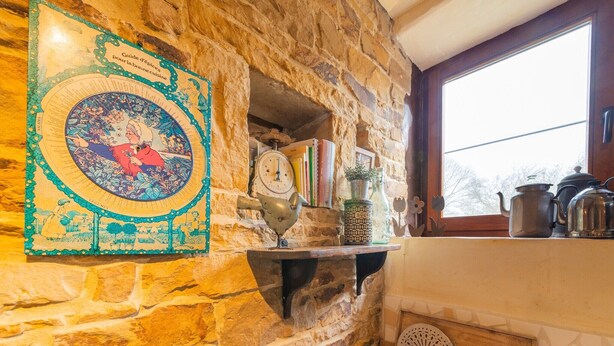A stone kitchen with a rustic charm, featuring a decorative plate, a scale, and kitchen utensils on the counter.