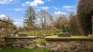 A stone wall garden with a wooden fence, a pathway, and a large tree in the background.