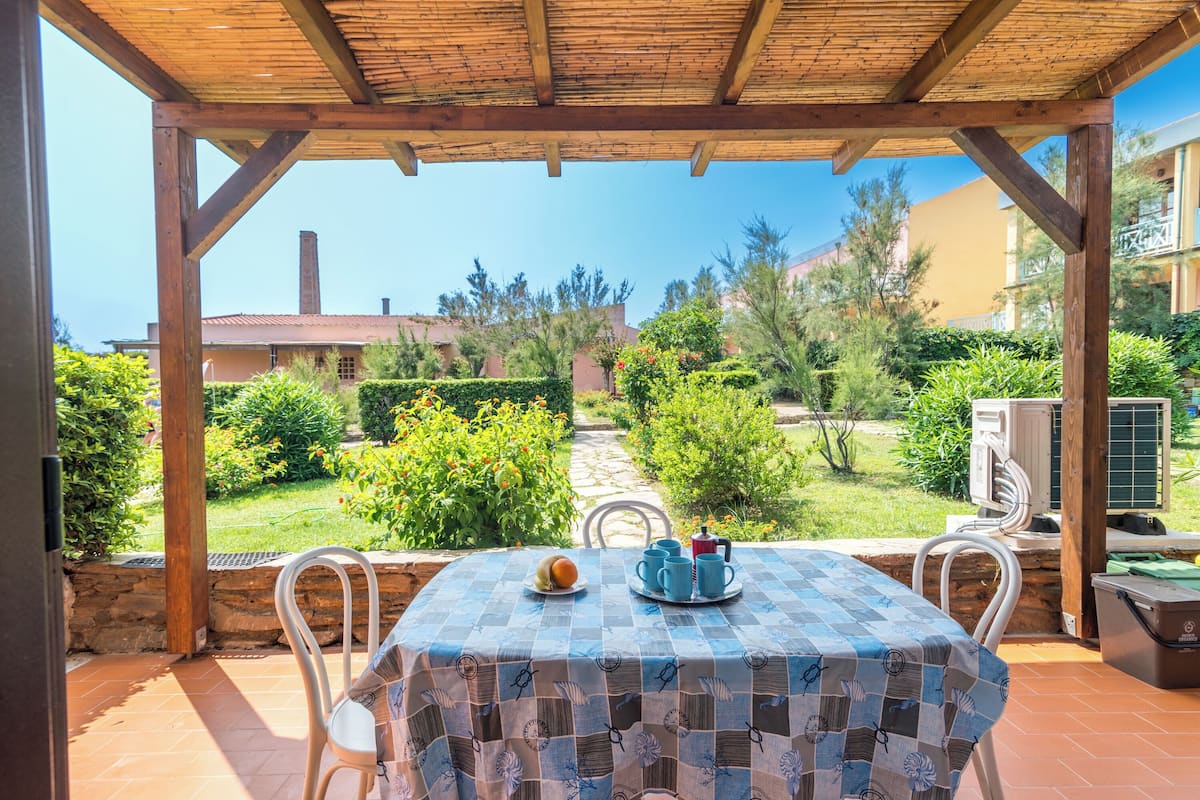 Une terrasse extérieure avec une table recouverte d’une nappe à carreaux, entourée de chaises blanches.
