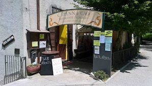 Un ristorante chiamato Capanna Cao con un cartello che indica che è una gelateria artigianale. Sono presenti aree con posti a sedere all'aperto, con tavoli e sedie, e un cartello per aperitivi al bar.