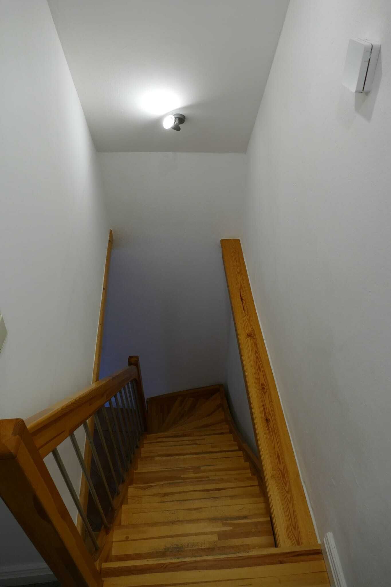 A wooden staircase with a handrail, white walls, and a ceiling light.