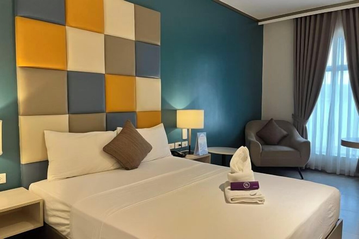 A hotel room with a bed, a nightstand, a chair, and a window with curtains.
