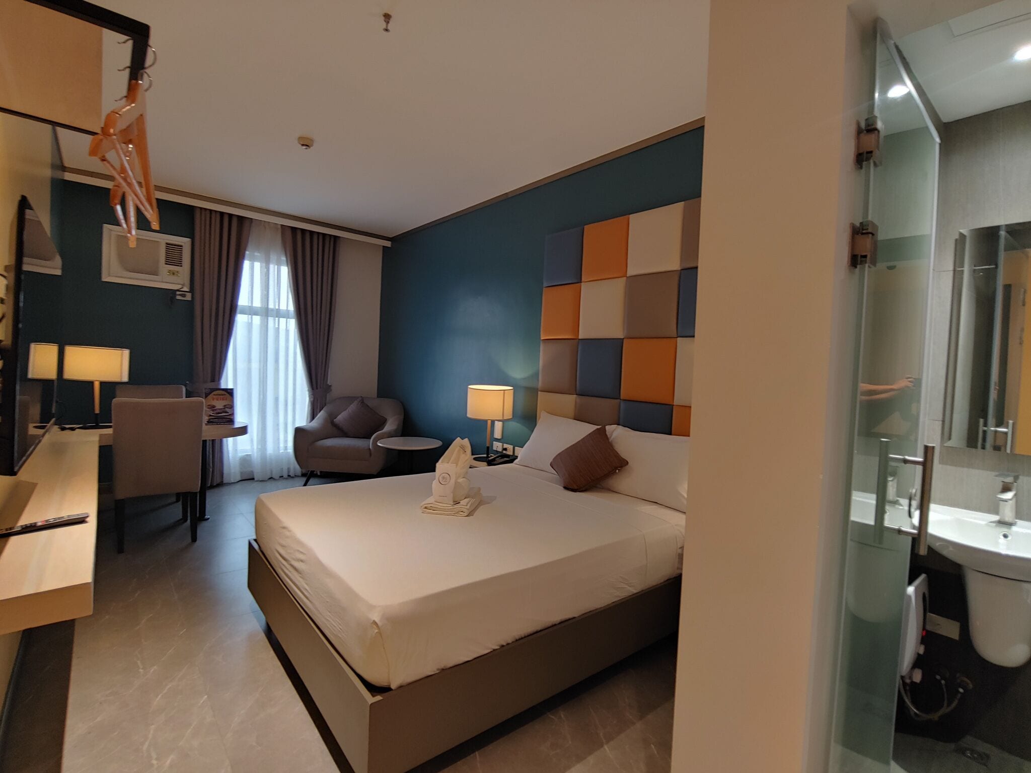 A hotel room with a bed, a desk, a chair, a lamp, and a bathroom.