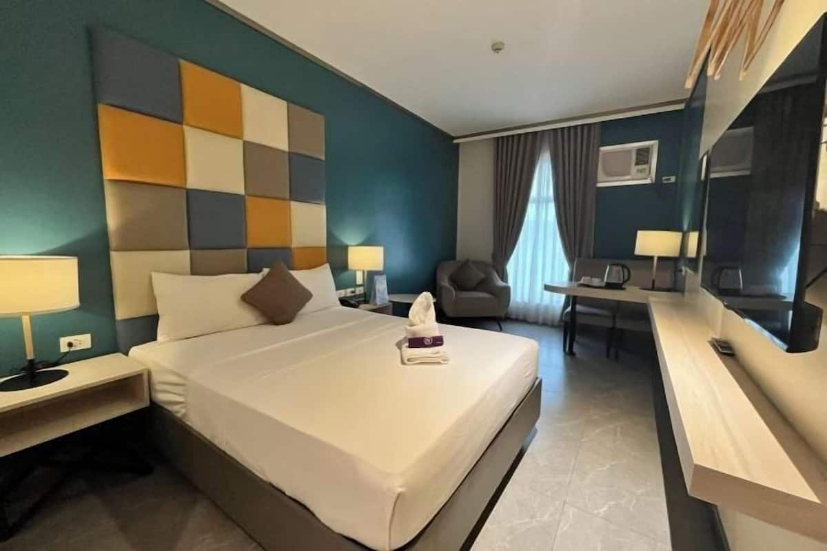 A hotel room with a large bed, bedside tables, a desk, a chair, and a mirror.