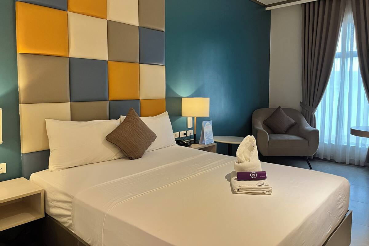 A hotel room with a bed, a nightstand, a chair, a lamp, and a window with curtains.