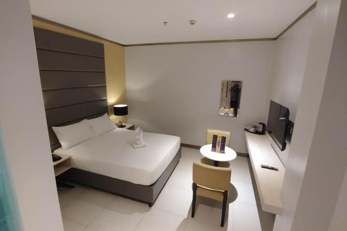 A modern hotel room with a bed, bedside table, chair, desk, and TV.
