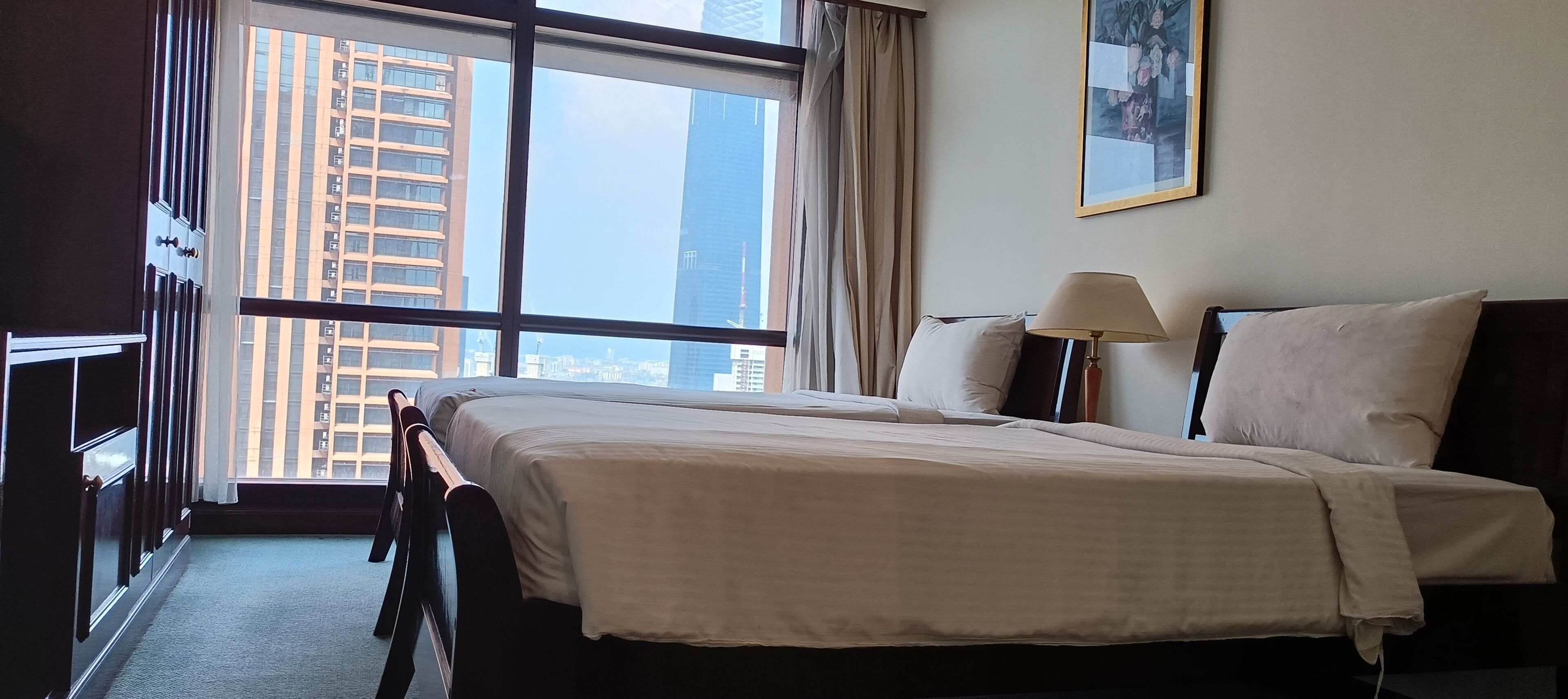 A hotel room with a large bed, a desk, a chair, a lamp, and a window with a city view.