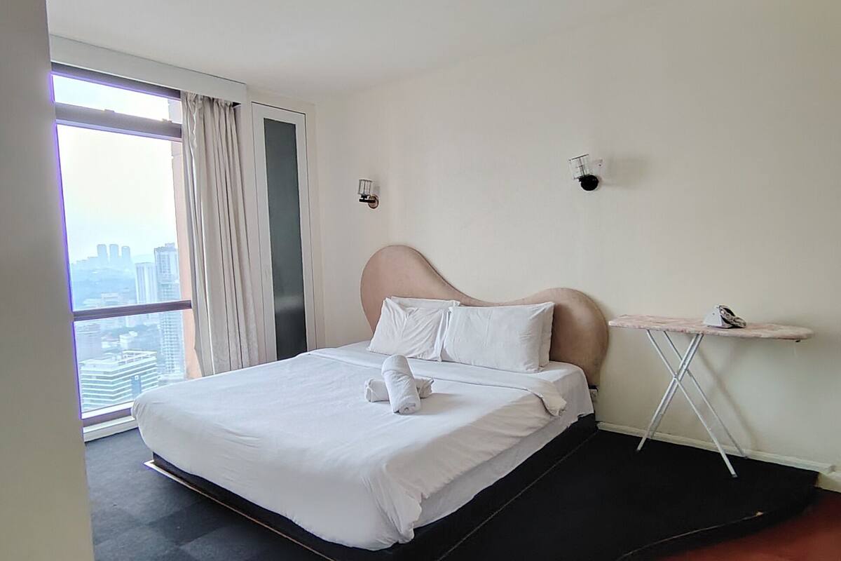 A hotel room with a bed, a small table, and a view of the city.