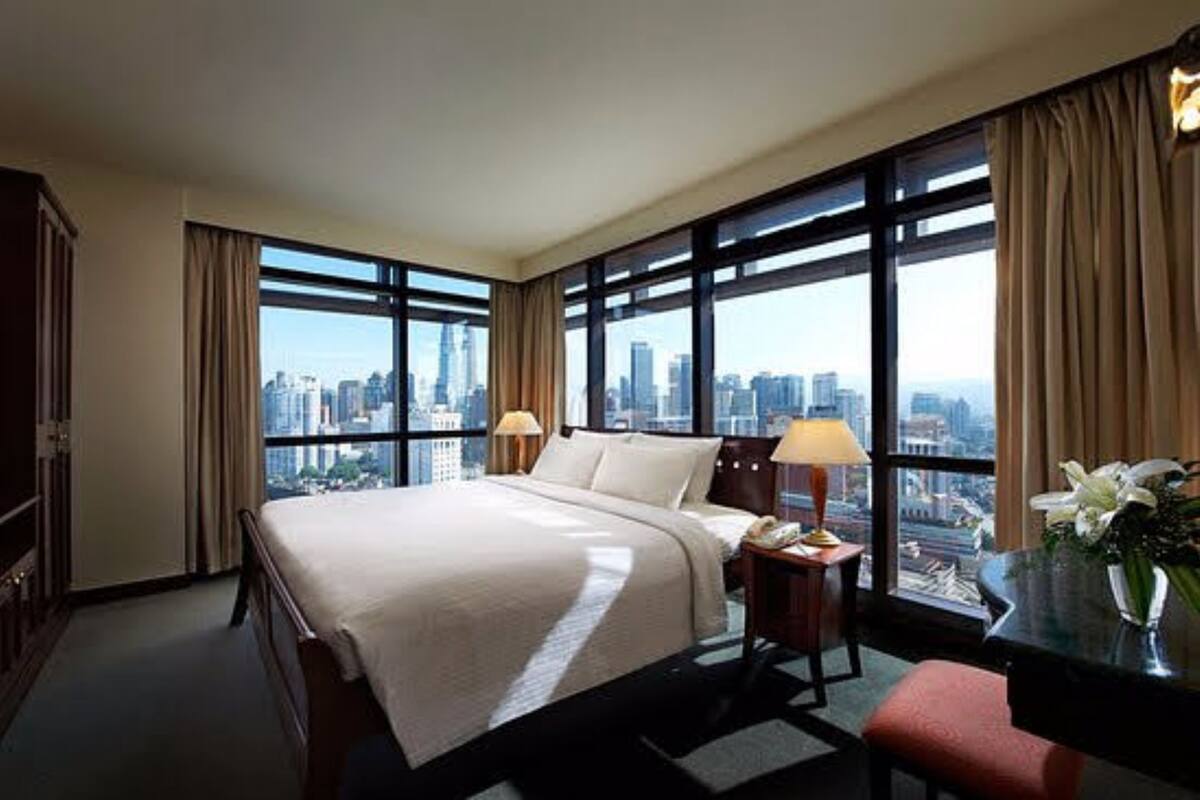 A hotel room with a large bed, two bedside tables, a desk, and a chair. The room has large windows with a city view.