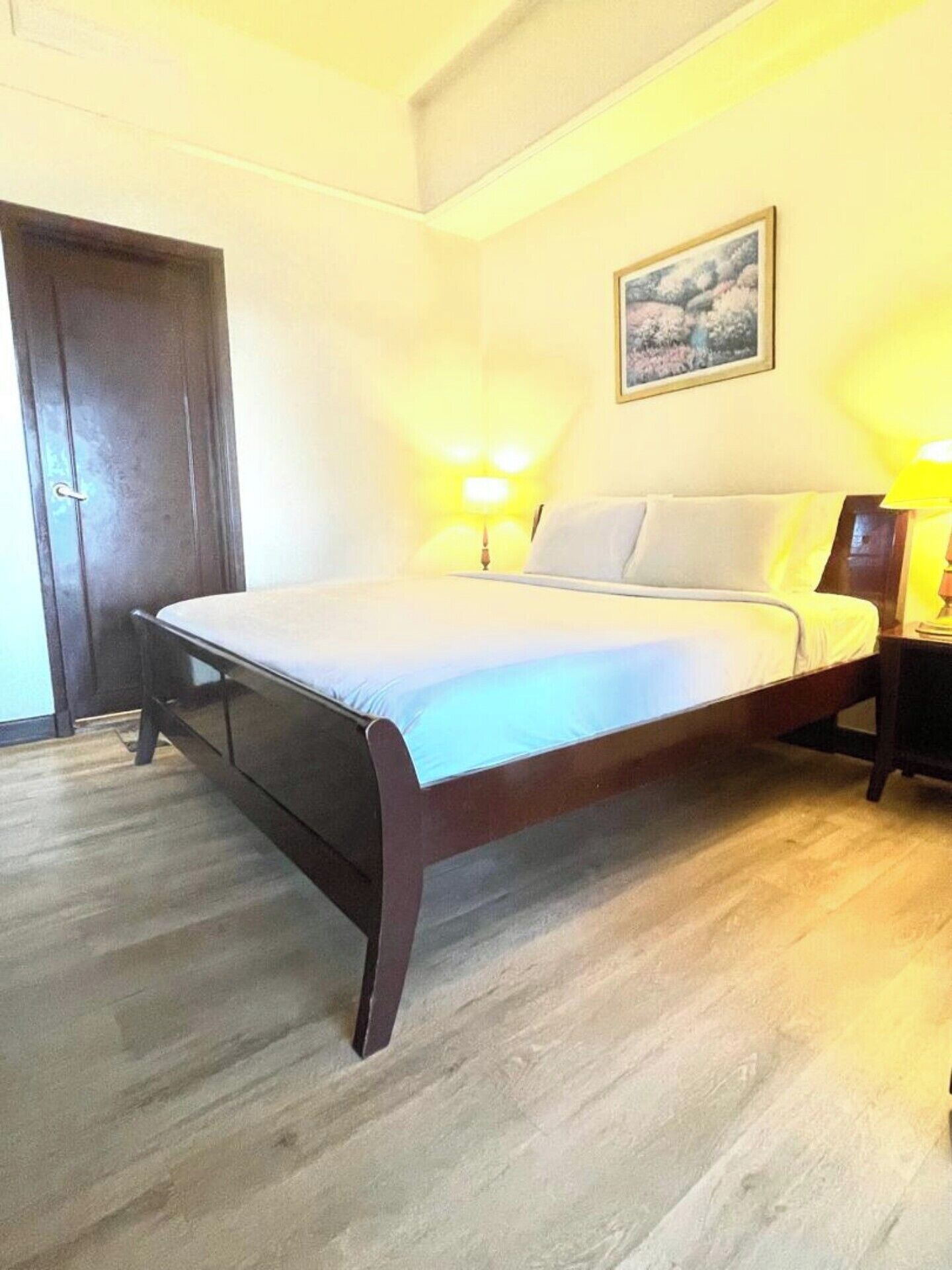 A bedroom with a bed, wooden floor, two bedside lamps, and a door.