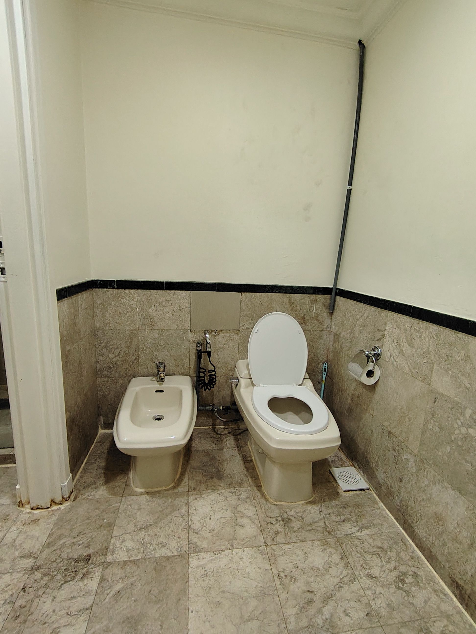 A small, tiled bathroom with a toilet and bidet, a towel rack, and a toilet paper holder.