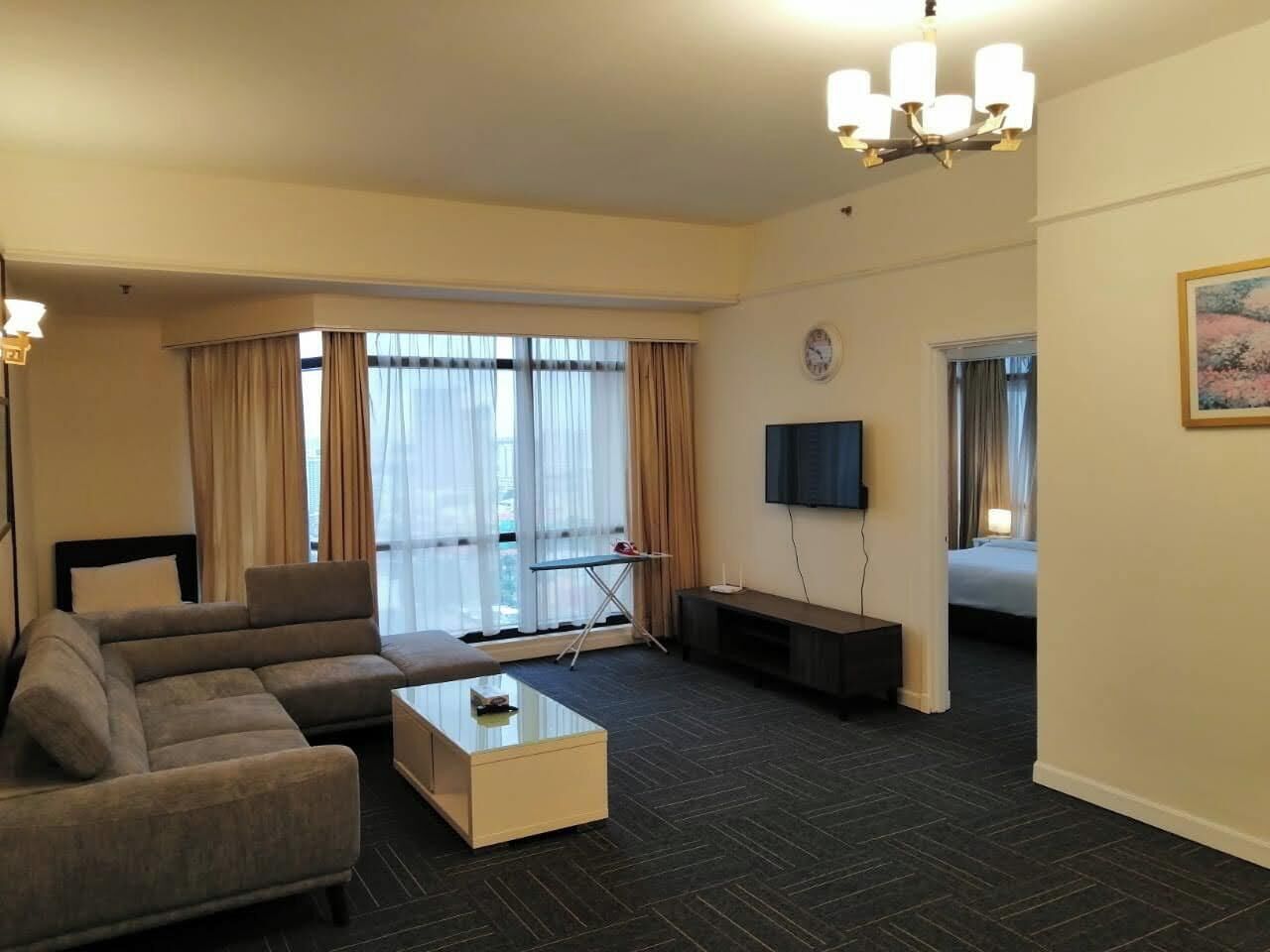 A modern hotel room with a sofa, coffee table, flat-screen TV, and a bed.