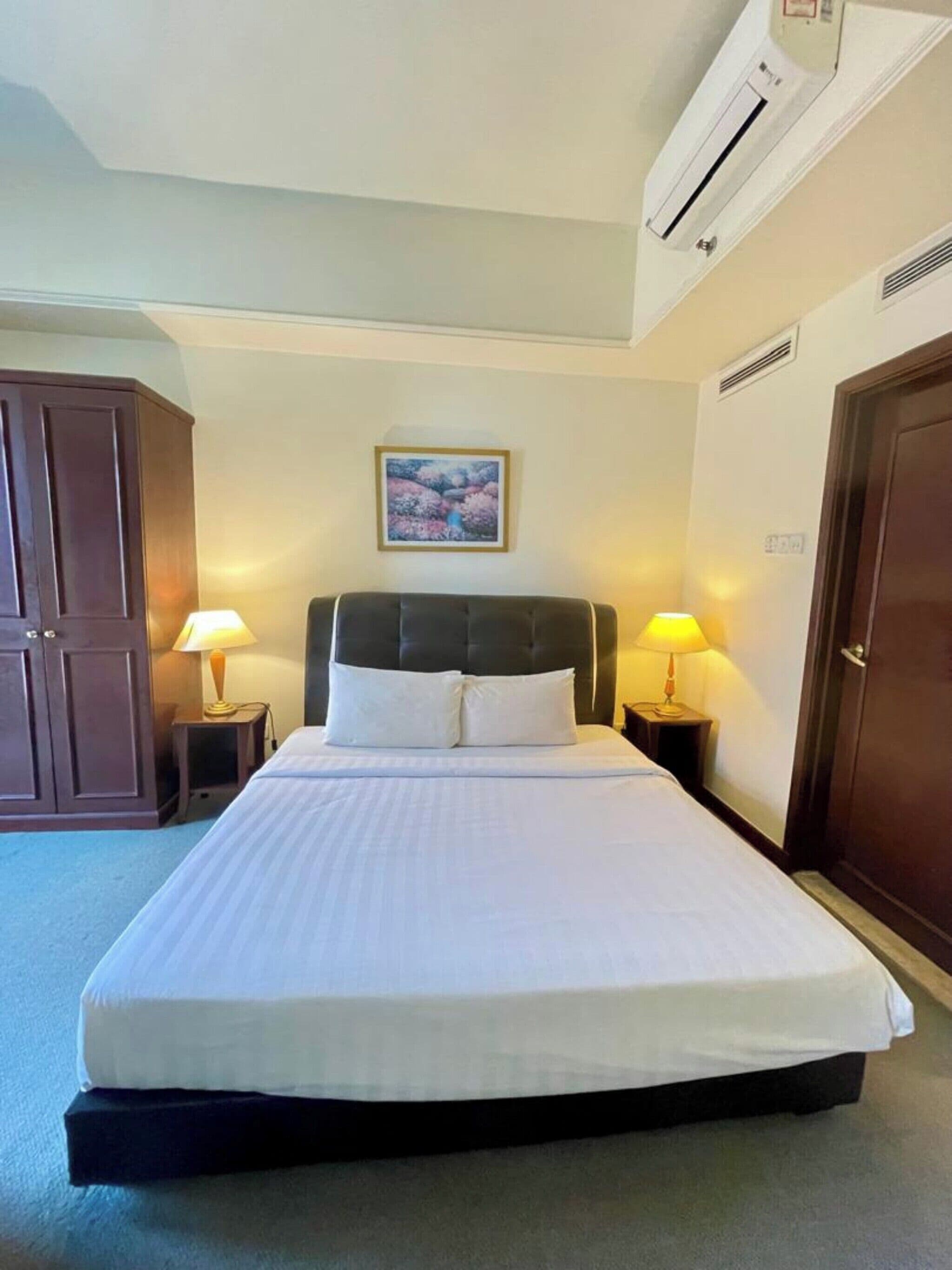 A hotel room with a large bed, two bedside lamps, a framed picture on the wall, and a wardrobe.