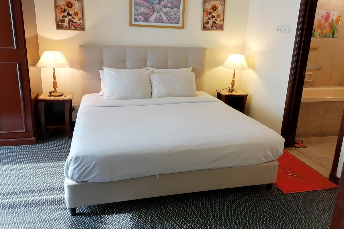 A hotel room with a large bed, two bedside lamps, and three framed floral paintings on the wall.