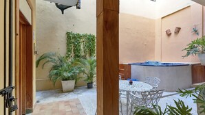 Ein Innenhof mit Fliesenboden, einem weißen Tisch mit Stühlen, Blumentöpfen und einem kleinen Wasserspiel.
