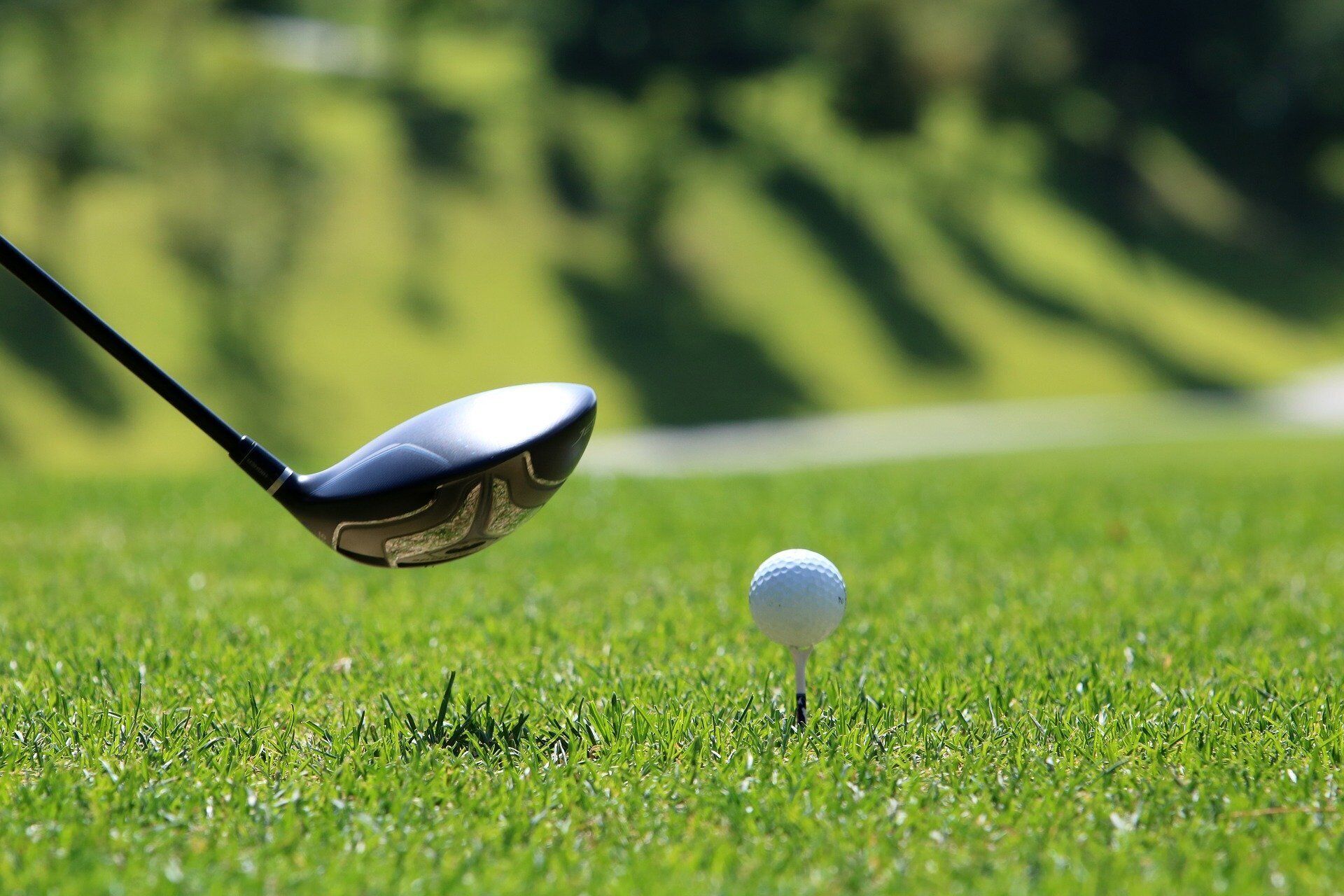 Un club de golf placé au-dessus d’une balle de golf sur un terrain herbeux.