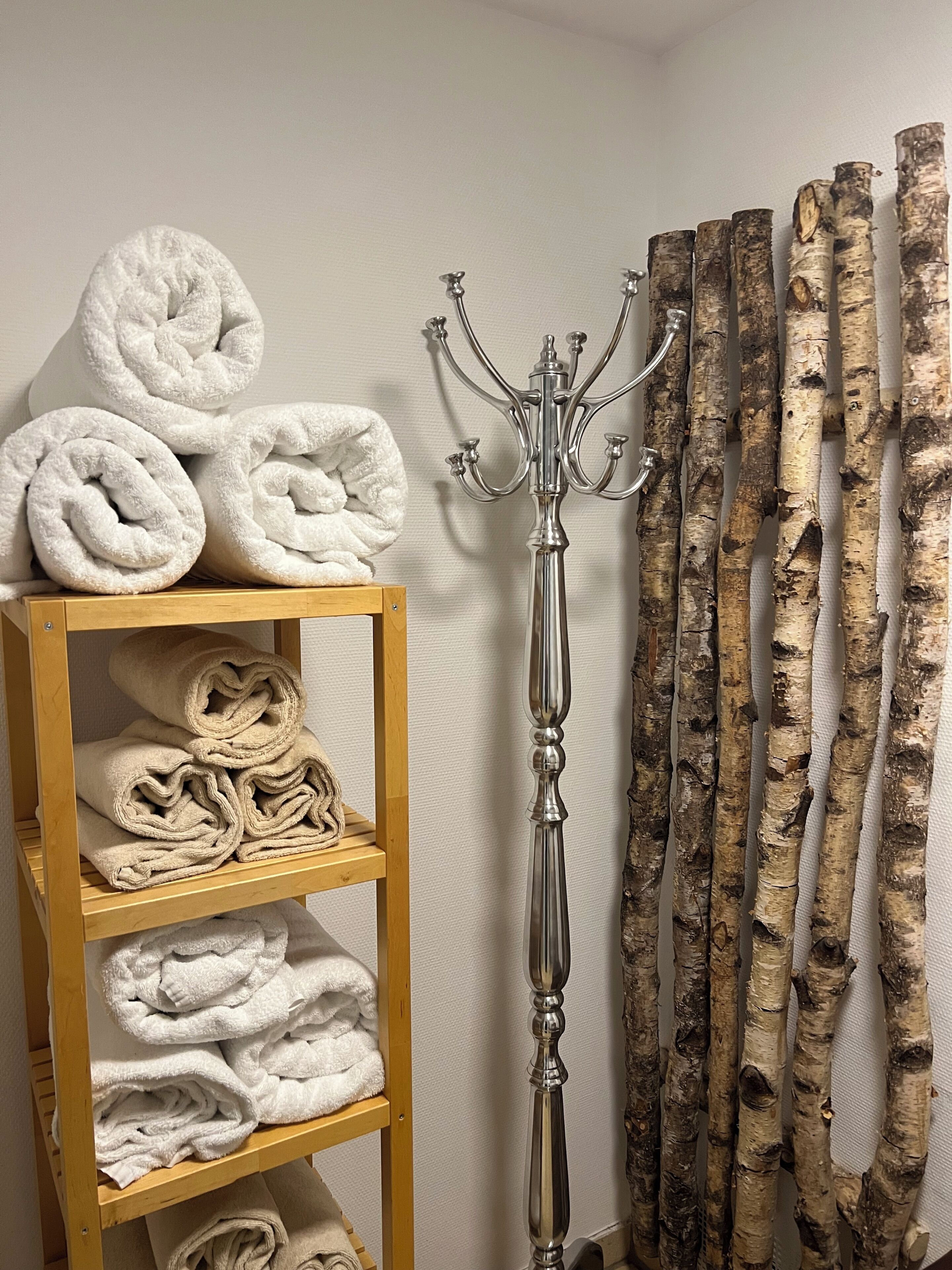 Un estante de madera con toallas dobladas con cuidado, un candelabro decorativo de metal y ramas de abedul sobre una pared lisa.