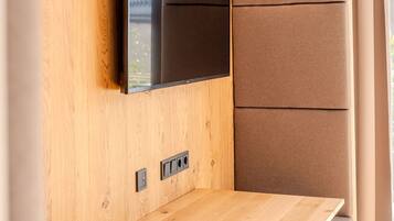 A modern RV interior with a flat-screen TV mounted on a wooden wall, a table, and a cushioned bench.