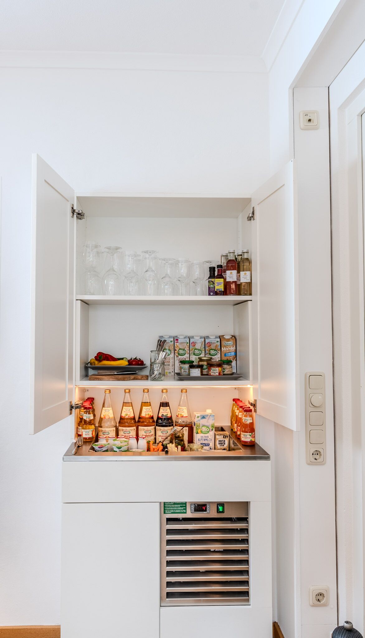 Un petit réfrigérateur doté de plusieurs étagères, contenant divers aliments, condiments et articles de verrerie.