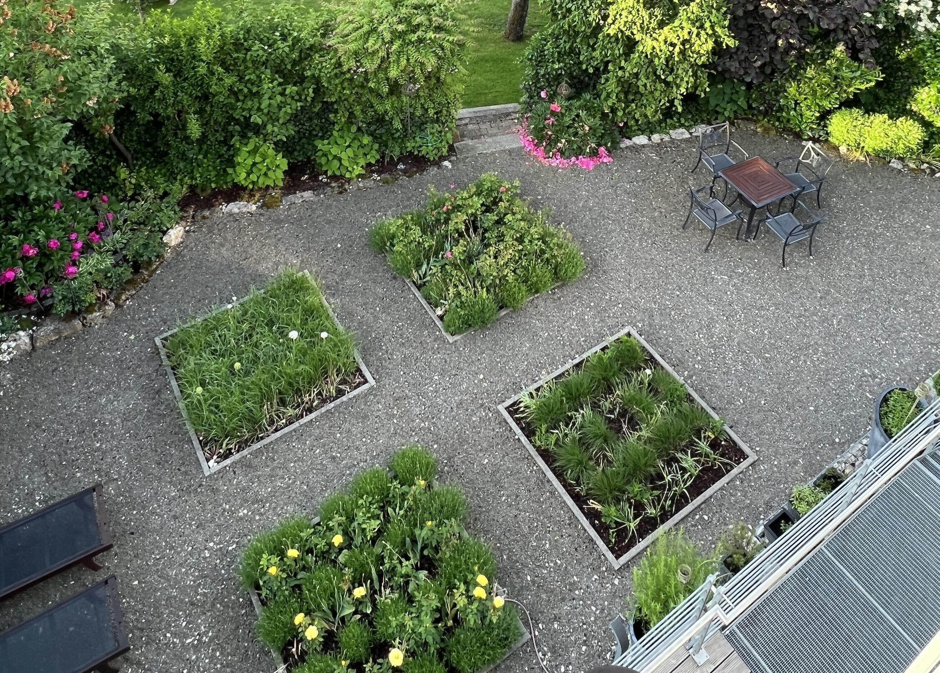 Un patio con varios maceteros cuadrados que contienen diversas plantas y flores.