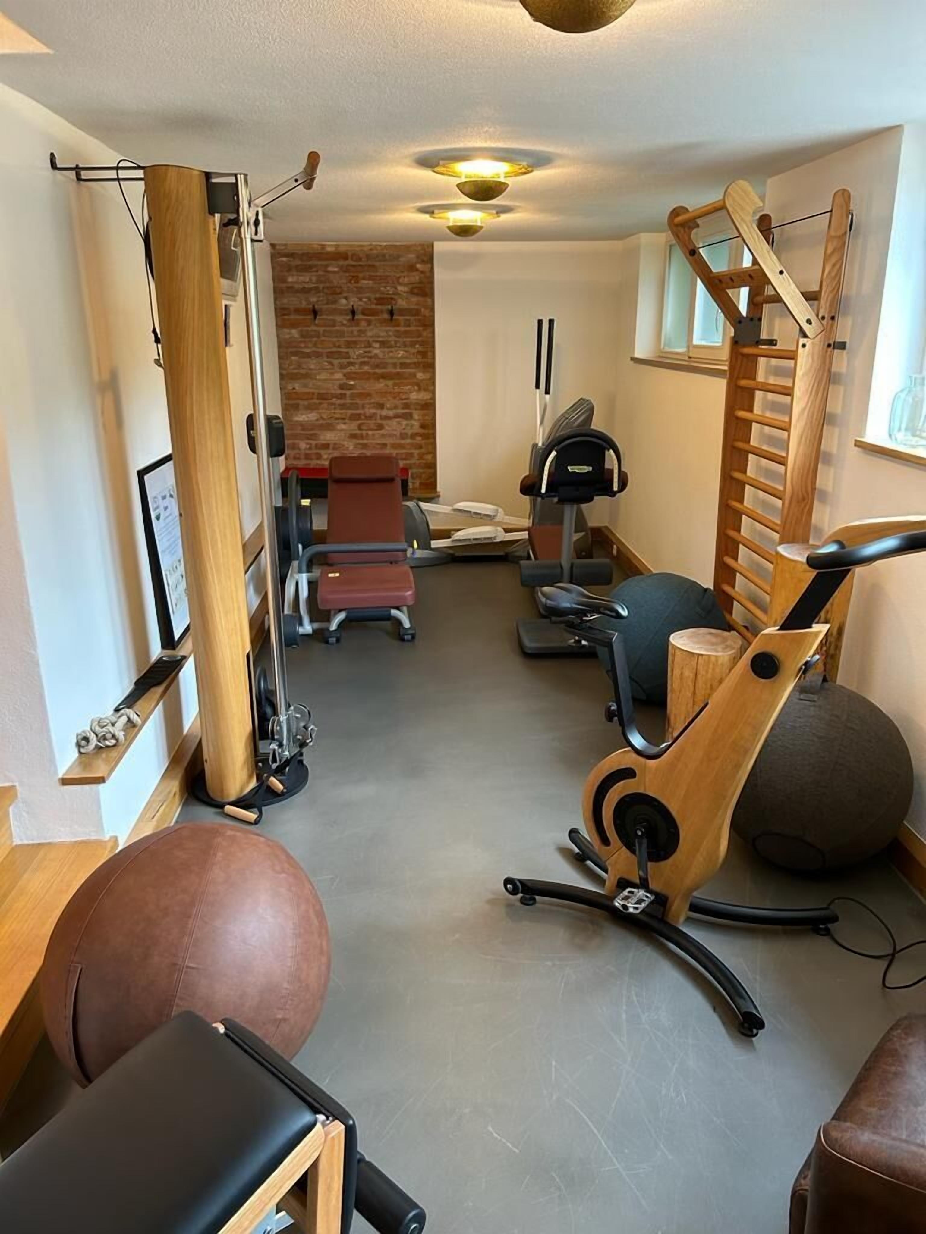 Un gimnasio en casa con equipo de ejercicio, una escalera de madera y un muro de ladrillo al fondo.