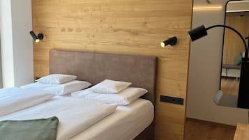 Un dormitorio moderno con cabecera de madera, cama con ropa blanca, dos lámparas de noche y un espejo en la pared.