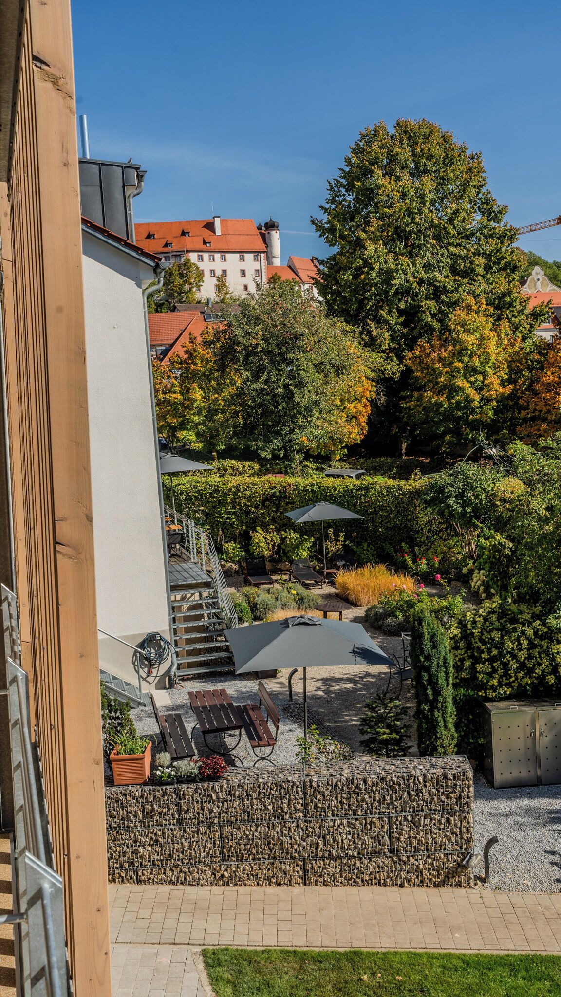 En gårdhave med udendørs siddepladser, en hæk og en bygning i baggrunden.