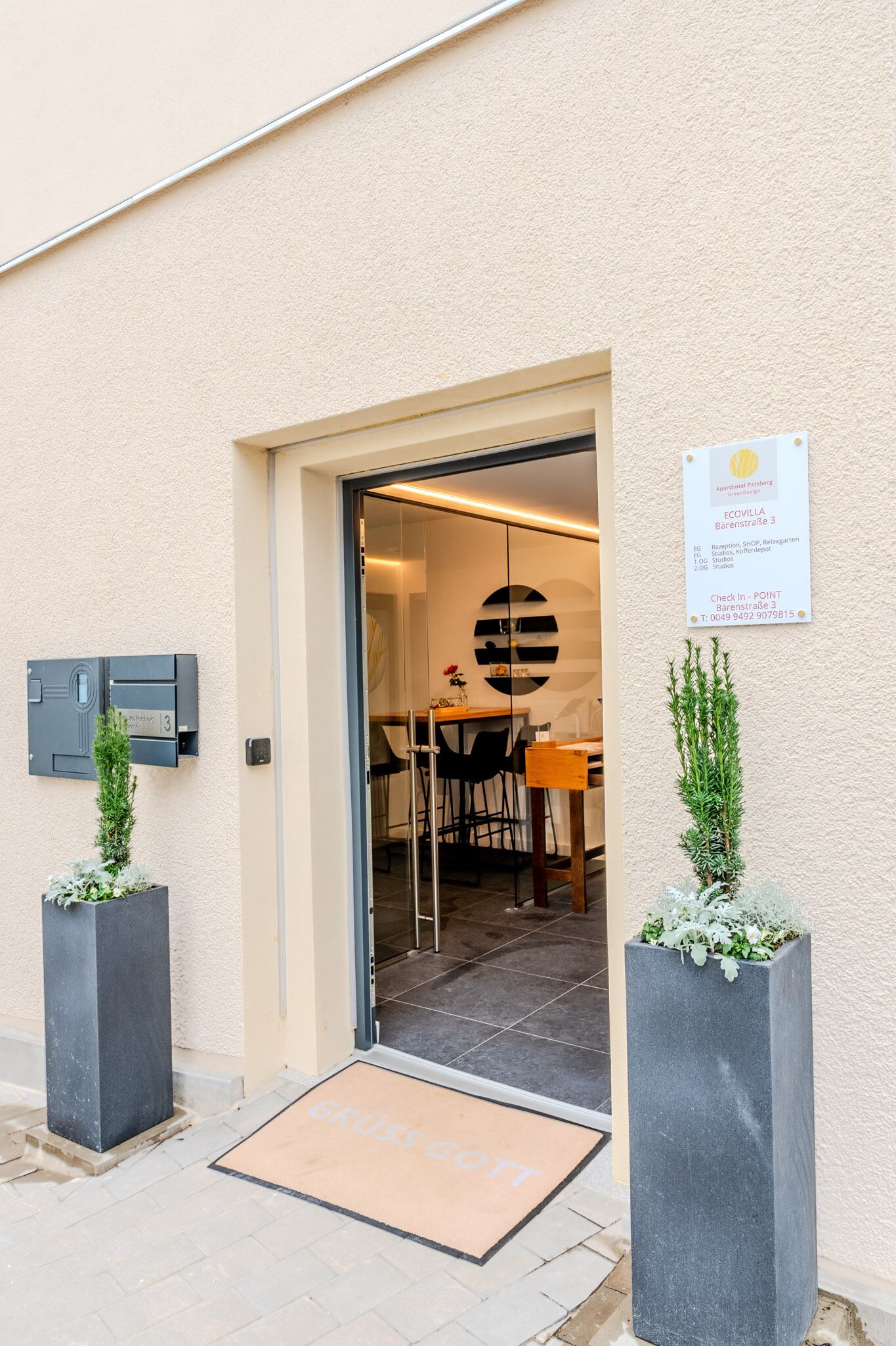 A hotel entrance with a reception desk, a glass door, and a sign indicating the location.
