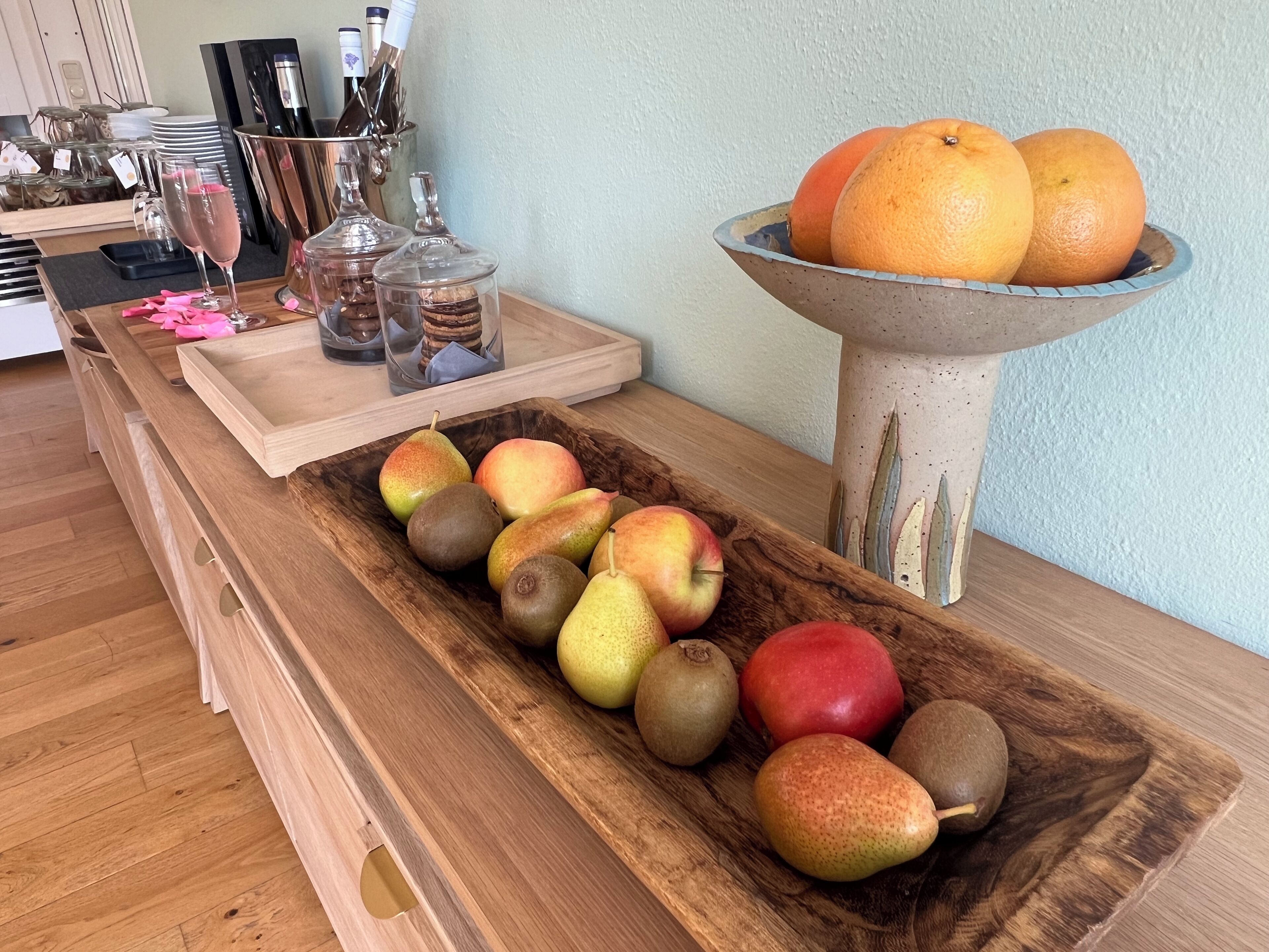 Een houten dienblad met verschillende soorten fruit en een decoratieve schaal vol sinaasappels op een tafel.