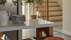 Un interior moderno con una escalera, una zona de comedor con mesa y sillas, y elementos decorativos como un mueble con patrones geométricos y una planta en maceta.