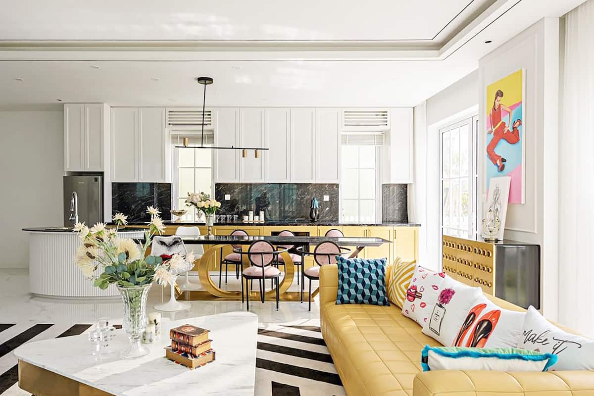 A modern living room with a yellow sofa, a dining area with a marble table, and a kitchen with white cabinets.
