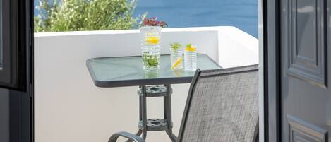 An open door leading to a balcony with a table and chairs, overlooking a body of water and distant land.