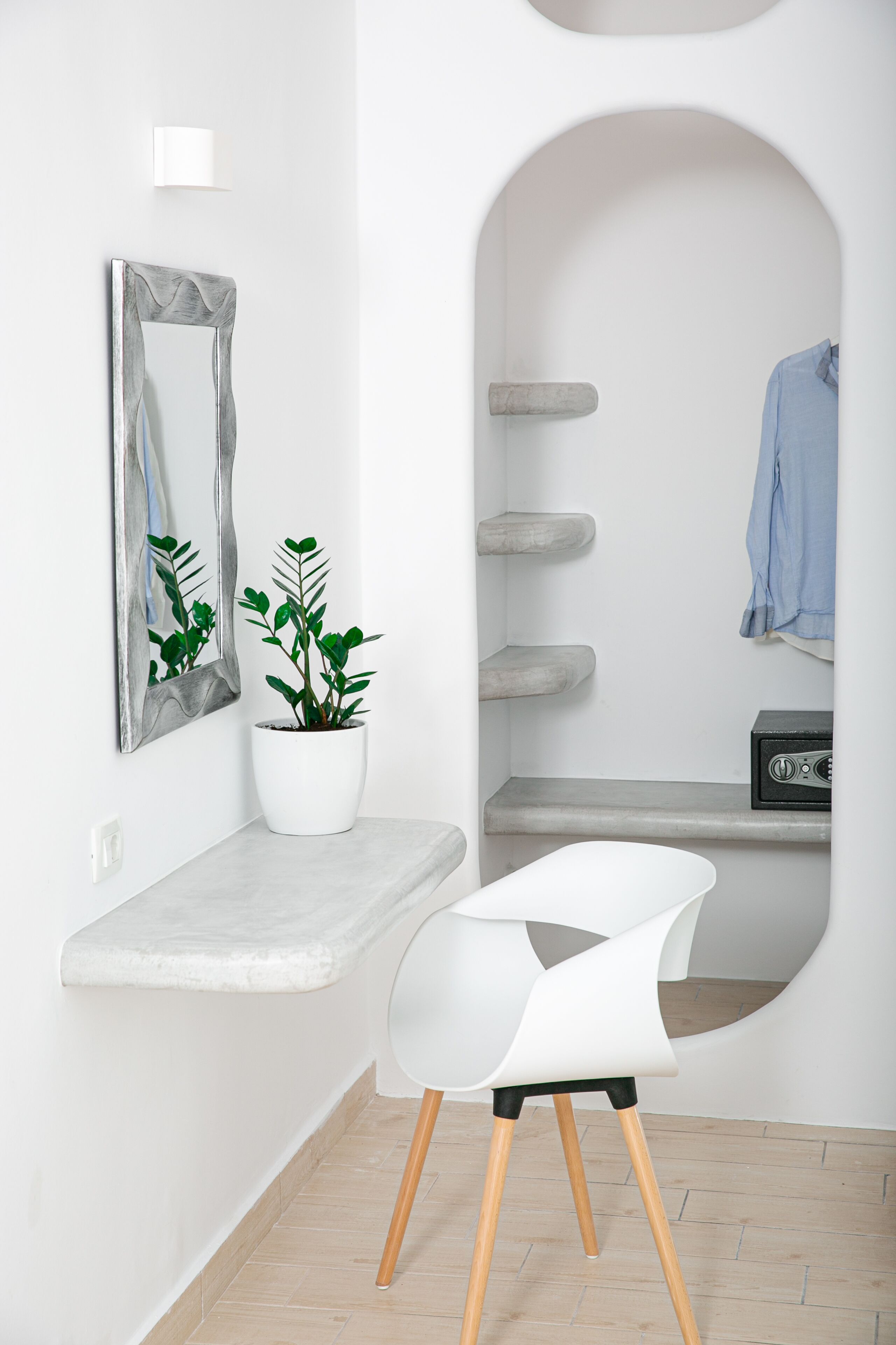 A modern bathroom with a white vanity, a potted plant, a white chair, and a mirror with a unique frame.