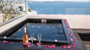 A hot tub with rose petals and champagne glasses, overlooking a coastal view. - Sensia (Santorini)