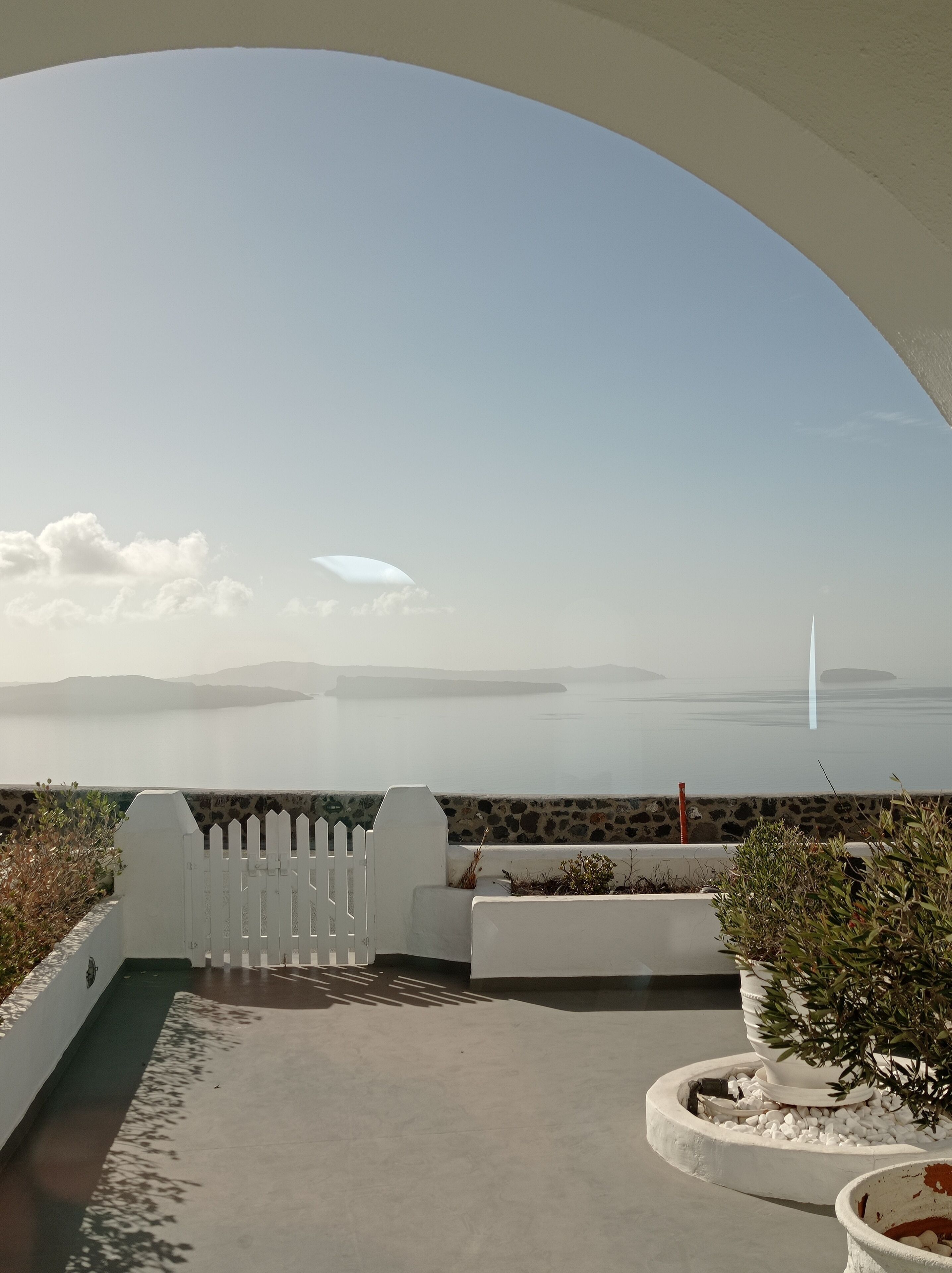 A terrace with a view of the sea, white railings, and potted plants.