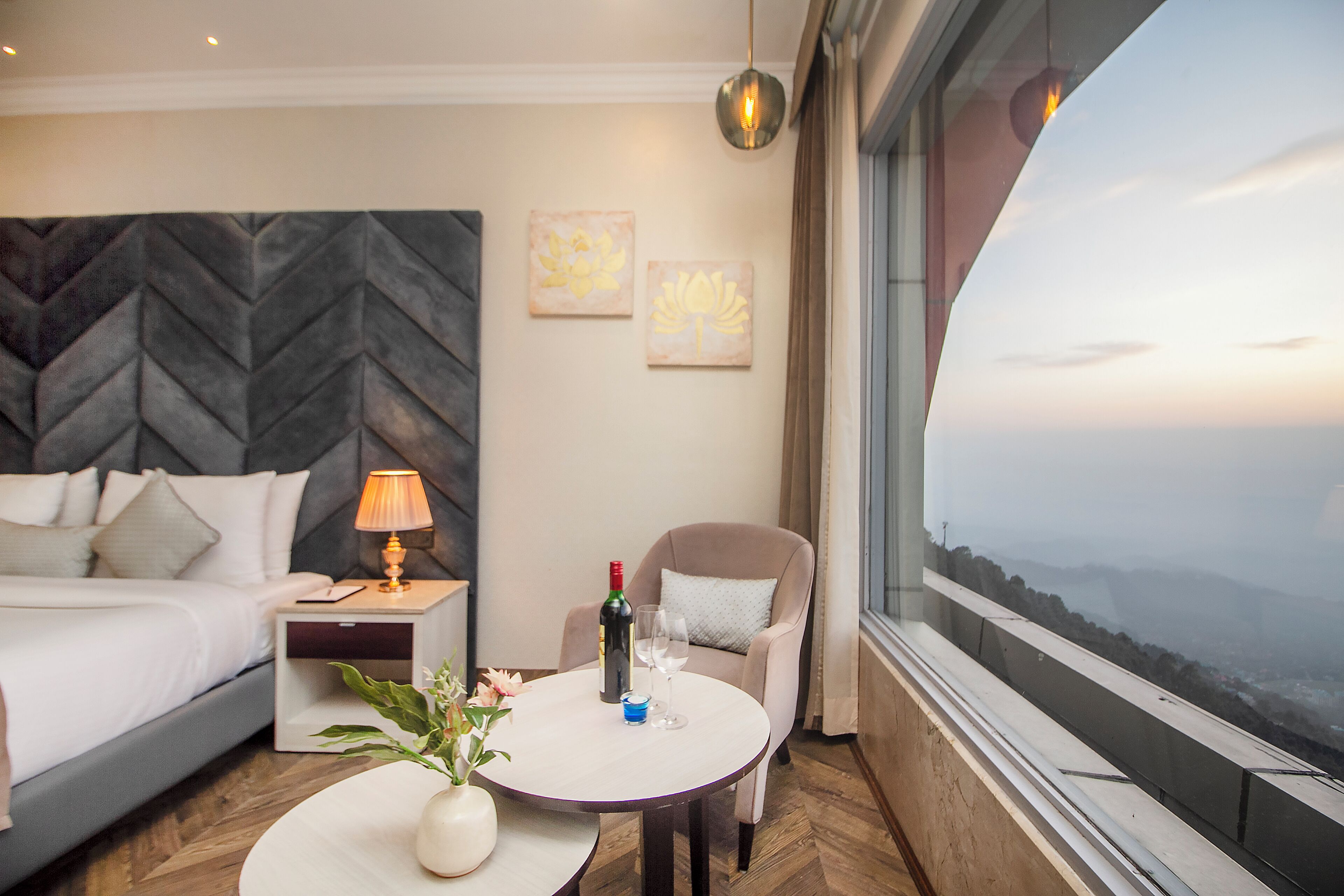 A hotel room with a bed, bedside table, lamp, chair, and a view of the landscape.