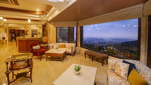 A spacious lobby with a reception desk, seating area, and large windows offering a city view. - Amritara Surya – A Luxury Spa Retreat (Dharamshala)