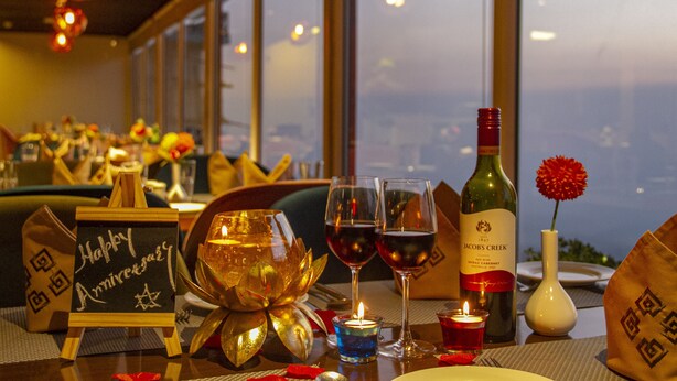 A restaurant table with a candle, wine glasses, a bottle of wine, and a 'Happy Anniversary' sign. - Amritara Surya – A Luxury Spa Retreat (Dharamshala)