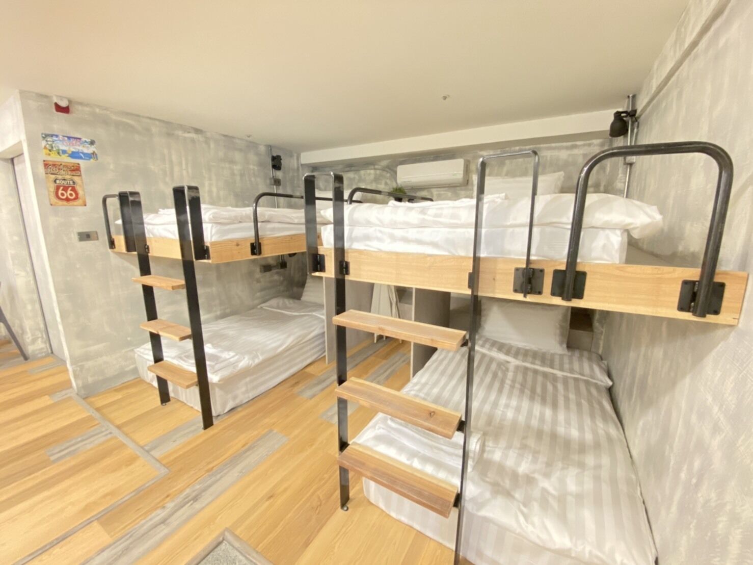 A bunk bed room with a wooden floor, metal railings, and a poster on the wall.