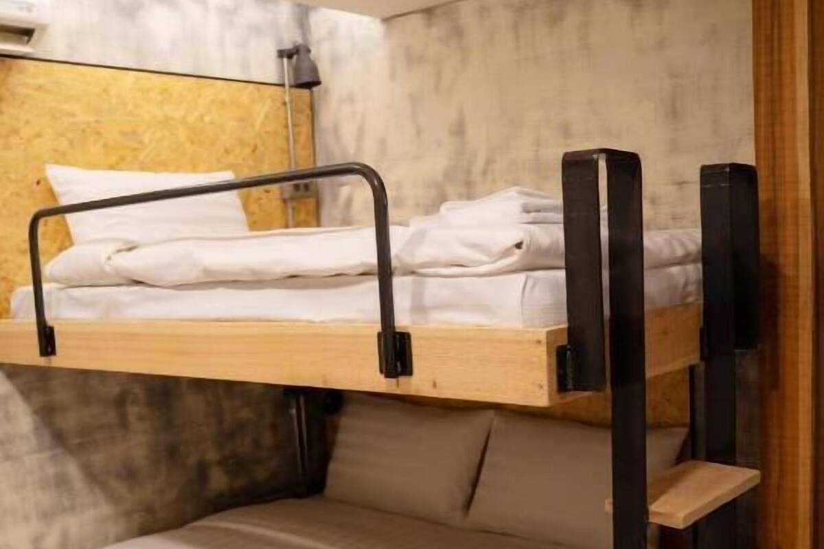 Ein Etagenbett mit Holzrahmen und einem Einzelbett darunter. Eine Regaleinheit ist an der Seite des Etagenbetts befestigt.